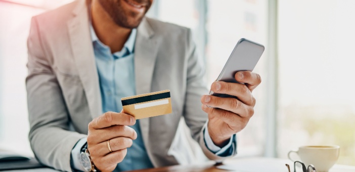 Hombre con celular en mano y tarjeta de crédito en la otra